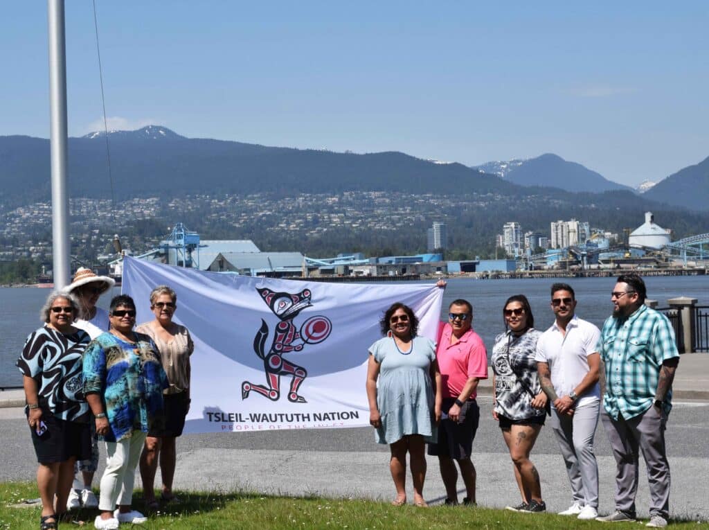 TWN Chief and Council members and staff stand with the TWN flag before it is permanently raised at spapəy̓əq Pápiy̓eḵ (Brockton Point), Stanley Park.
