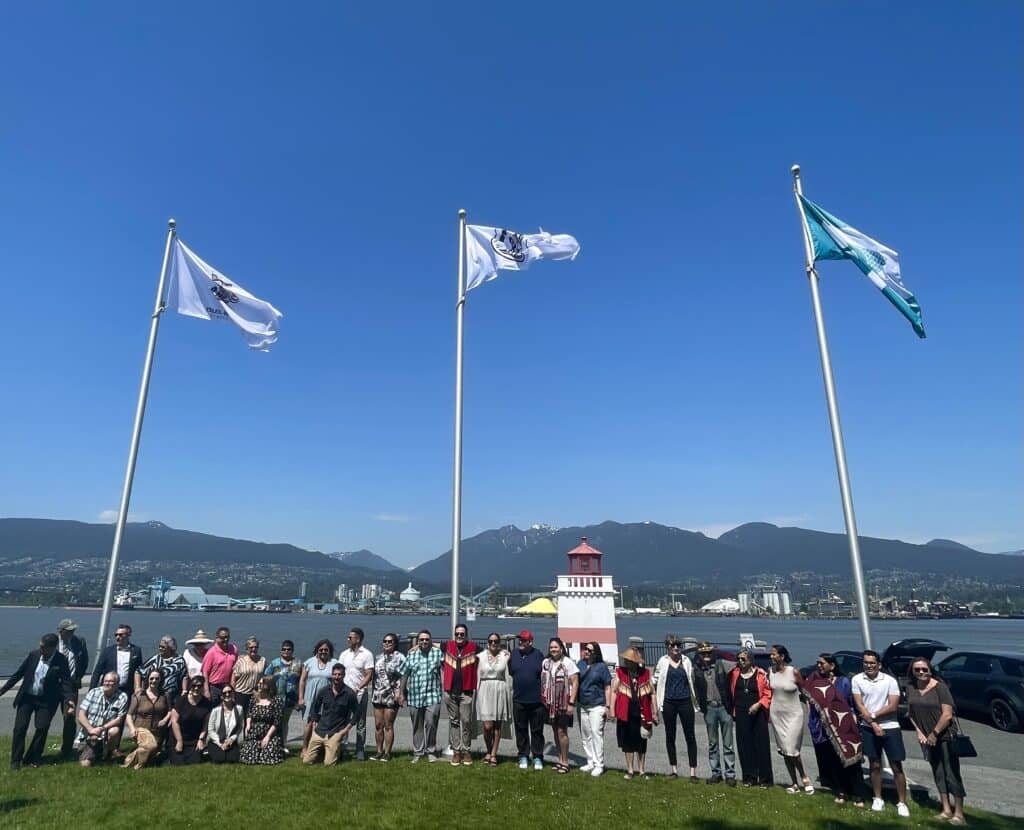 Elected leadership and staff from Musqueam, Squamish, and Tsleil-Waututh Nations stand with the Vancouver Park Board in front of MST flags.